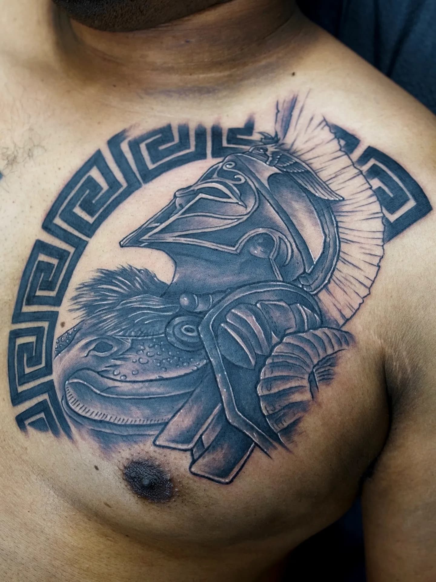 Black and grey Spartan helmet tattoo with geometric pattern on chest