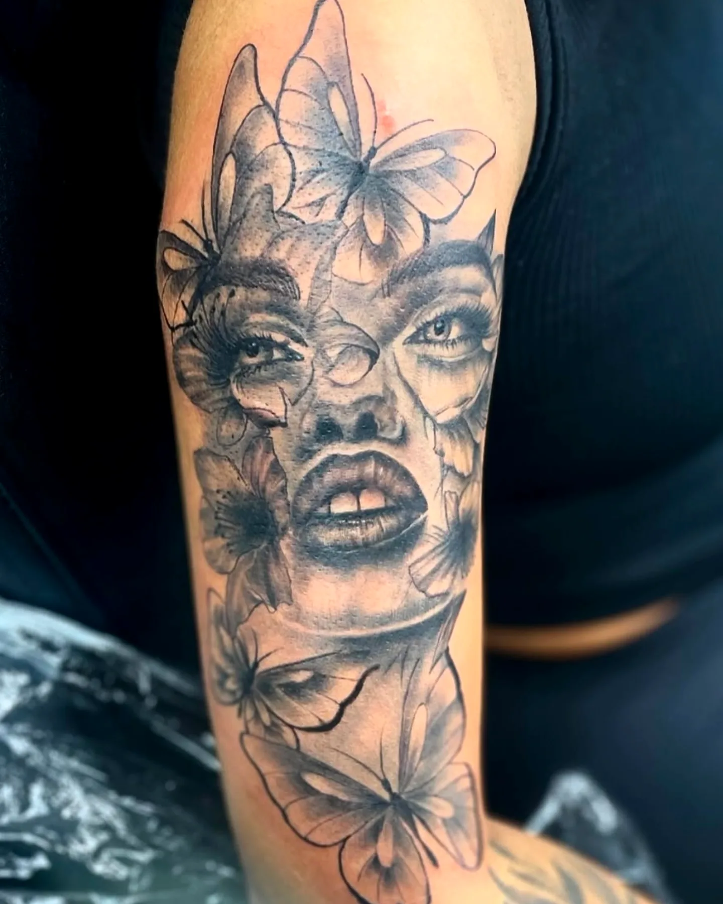 Black and grey portrait of a woman surrounded by butterflies on upper arm
